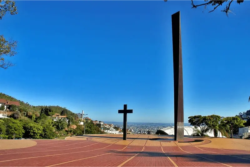 Imagem da Praça Governador Israel Pinheiro, mais conhecida como Praça do Papa. A imagem mostra a cruz e o obelisco da praça com o horizonte no plano de fundo, em um dia ensolarado e sem nuvens
